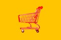 Shopping trolley in the store. Red basket on a yellow background. The concept of retail, sale of goods and products.