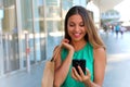 Shopping woman using smartphone and holding bag while standing on the mall background. Attractive young woman texting