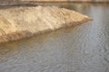 The shore of an artificial pond. A mound of sand on the water.