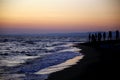 The shore illuminated by the light of the sunset with standing silhouettes of people