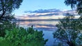 On the shore of the lake grows grass, bushes, and trees, with branches leaning over the water. During sunset, the colorful sky wit Royalty Free Stock Photo