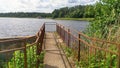 On the shore of the lake next to the alder made concrete pier with a metal fence. In the water - reeds, on the water - the wave. O Royalty Free Stock Photo