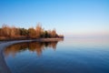 The shore of the reservoir. Sandy beach, autumn forest in the rays of the setting sun, calm expanse of water without waves