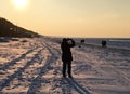 On the shore of the snowy Gulf of Riga, a woman photographs the sunset. Latvia, March 2018 Royalty Free Stock Photo