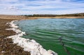 Shore of the ValdecaÃÂ±as reservoir with green pollution in the water and a white foam on the shore