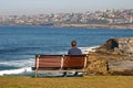 Man sitting on wood bench looking at panorama of idyllic and amazing seaside landscape of jagged shore, rocks, hillside buildings Royalty Free Stock Photo