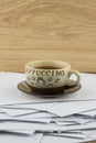 Short break at the hard worker: a Cup of hot coffee and a brown glass saucer on a disorderly stack of papers, side view from above Royalty Free Stock Photo