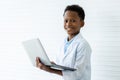Short haired african american boy in white lab coat holding computer laptop in both hands. He smiled happily as he prepared and