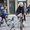 Short-haired blonde girl with a bicycle and an elderly man with a cane cross the road on a pedestrian crossing