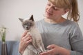 A short-haired cat with a displeased muzzle in the hands of a white Caucasian woman. From a low angle view indoors