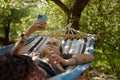 Young diverse woman with short hair lying on a hammock in a park and browsing mobile app on a smartphone. Stylish tattooed female Royalty Free Stock Photo