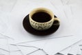 Short rest at the hard worker: a Cup of hot coffee and a brown ceramic saucer on a disorderly stack of papers, a side view from Royalty Free Stock Photo