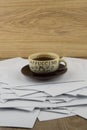 Short rest at the hard worker: a Cup of hot coffee and a brown ceramic saucer on a disorderly stack of papers, a side view from Royalty Free Stock Photo