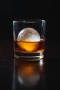 Short Rocks Glass with Deep Amber Drink and Flawless Ice Sphere Under Light Royalty Free Stock Photo