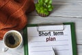 SHORT TERM PLAN - text in a notebook with a pen, a cactus, a cup of coffee and a fragment of a brown plaid