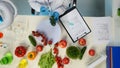 In the shot above, a scientist is sitting. Around her on the table are vegetables and laboratory supplies. She is