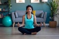 African attractive sporty young woman doing yoga and hypopressive exercises while staying in lotus position in living room at home Royalty Free Stock Photo