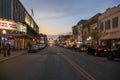 A shot along Broughton Street lined with restaurants, shops, black light posts, bare trees and people standing with cars