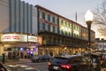 A shot along Broughton Street lined with restaurants, shops, black light posts, bare trees and people standing with cars