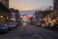 A shot along Broughton Street lined with restaurants, shops, black light posts, bare trees and people standing with cars