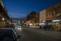 A shot along Broughton Street lined with restaurants, shops, black light posts, bare trees and people standing with cars