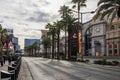 A shot along Las Vegas Blvd with cars driving on the street, hotels and restaurants, people walking, tall lush green palm trees