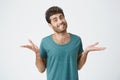 Shot of attractive bearded grinning man dressed in blue T-shirt, telling he doesn t know what to do. Clueless and Royalty Free Stock Photo