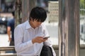 Shot of an attractive Japanese young man using his cellphone while waiting at bus stop.