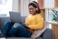 Home is my happy place. Shot of an attractive young woman wearing headphones while using her laptop. Royalty Free Stock Photo