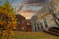 A shot of an autumn landscape with a red brick building next to a concrete building with fallen autumn leaves on grass Royalty Free Stock Photo