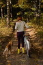 Shot from the back of a young woman walking her dog in the autumn forest and riding a bike. Royalty Free Stock Photo