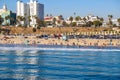 A shot of beach front hotels with lush green palm trees and parked cars near a sandy beach with people relaxing Royalty Free Stock Photo