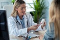 Beautiful mature female doctor talking while explaining medical treatment while prescribing medication to patient in the Royalty Free Stock Photo