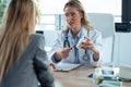 Beautiful mature female doctor talking while explaining medical treatment while prescribing medication to patient in the Royalty Free Stock Photo