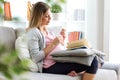 Beautiful pregnant woman reading a book and eating yogurt on the sofa at home.