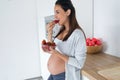 Beautiful pregnant young woman eating strawberries out of bowl in the kitchen at home Royalty Free Stock Photo