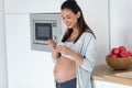 Beautiful pregnant young woman eating yogurt while standing in the kitchen at home Royalty Free Stock Photo