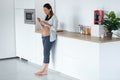 Beautiful pregnant young woman eating yogurt while standing in the kitchen at home Royalty Free Stock Photo