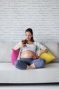 Beautiful pregnant young woman using her mobile phone while eating strawberries on sofa at home Royalty Free Stock Photo