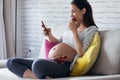 Beautiful pregnant young woman using her mobile phone while eating strawberries on sofa at home Royalty Free Stock Photo