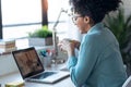 Beautiful young afro business woman making video call with laptop while drinking coffee sitting in the office at home Royalty Free Stock Photo