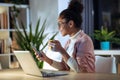 Beautiful young entrepreneur woman using her smart phone while drinking a cup of coffee sitting in the office Royalty Free Stock Photo