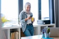 Beautiful young muslim business woman wearing hijab using her smart phone while standing next to the window in the office Royalty Free Stock Photo