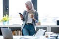 Beautiful young muslim business woman wearing hijab using her smart phone while standing next to the window in the office Royalty Free Stock Photo
