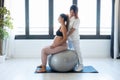 Beautiful young physiotherapist helping to beautiful pregnant woman for doing pilates exercises with ball preparing for childbirth