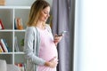 Beautiful young pregnant woman texting with her smartphone at home Royalty Free Stock Photo