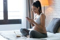 Beautiful young pregnant woman using her mobile phone while eating cereals and sitting on the bed at home Royalty Free Stock Photo