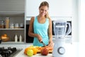 Beautiful young sporty woman cutting some vegetables and fruits while listening to music in the kitchen.