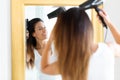 Beautiful young woman blow drying her hair near the mirror in the bathroom Royalty Free Stock Photo