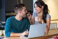 Shot of beautiful young woman giving yogurt to her handsome boyfriend while they surfing in internet with laptop in the kitchen.